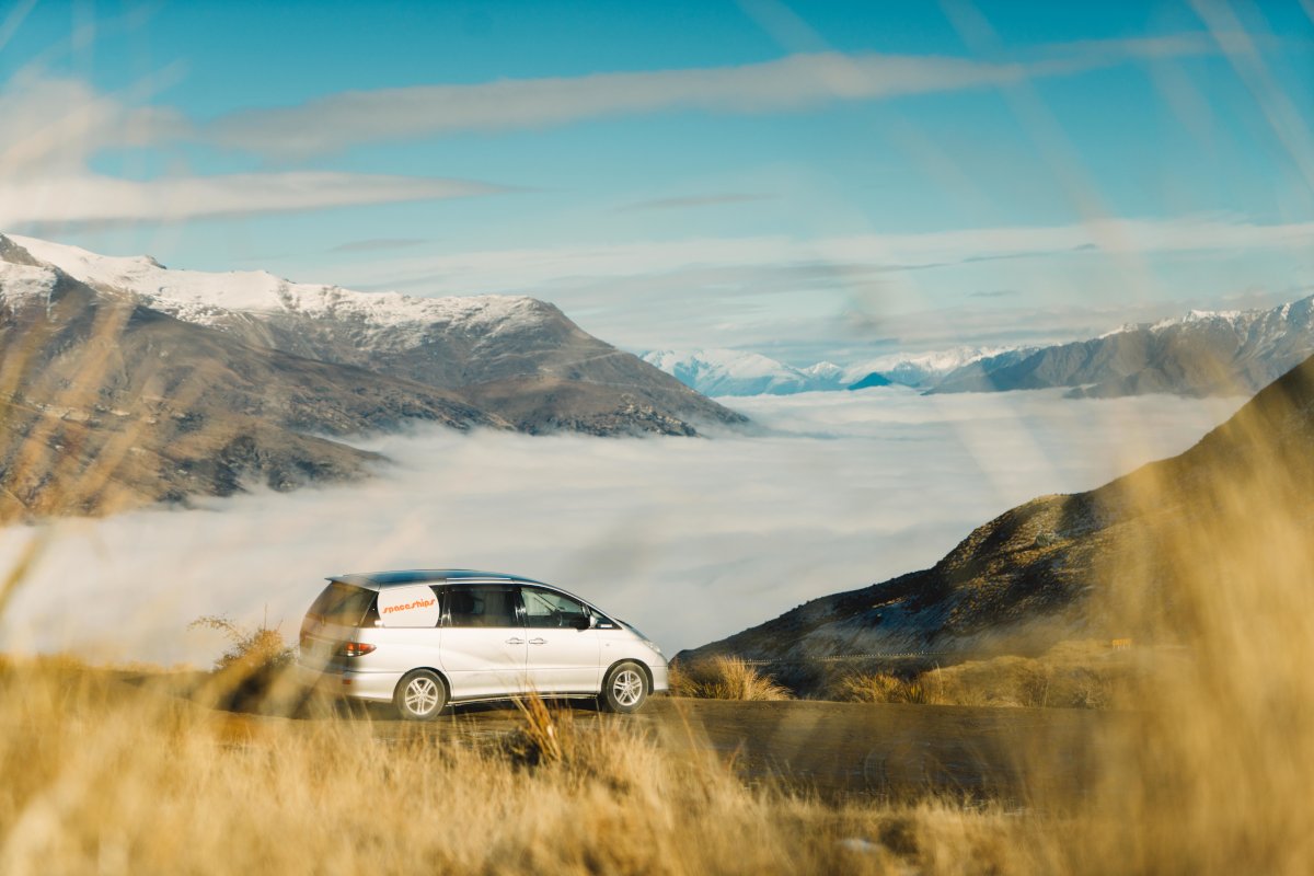 Campervan driving on a mountain ridge road overlooking the mountain range above the clouds