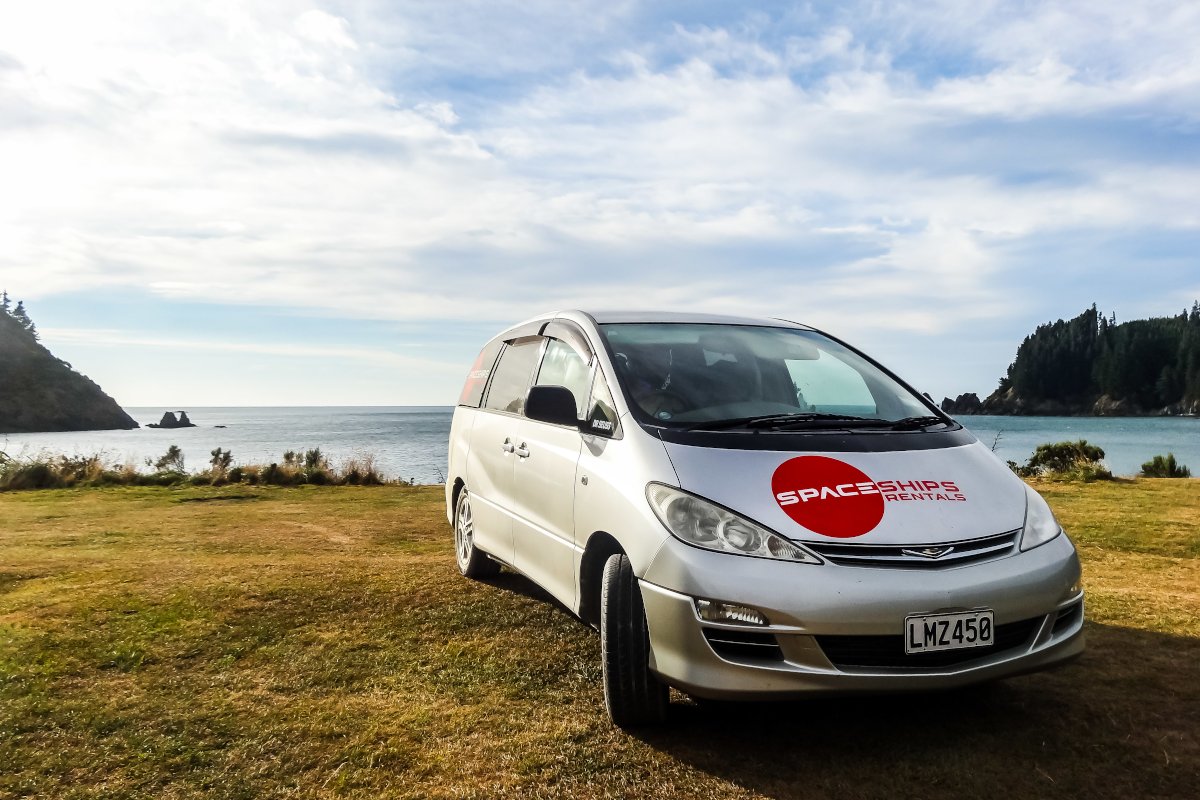 Silver campervan parked on the grass in front of the ocean with headlands on either side