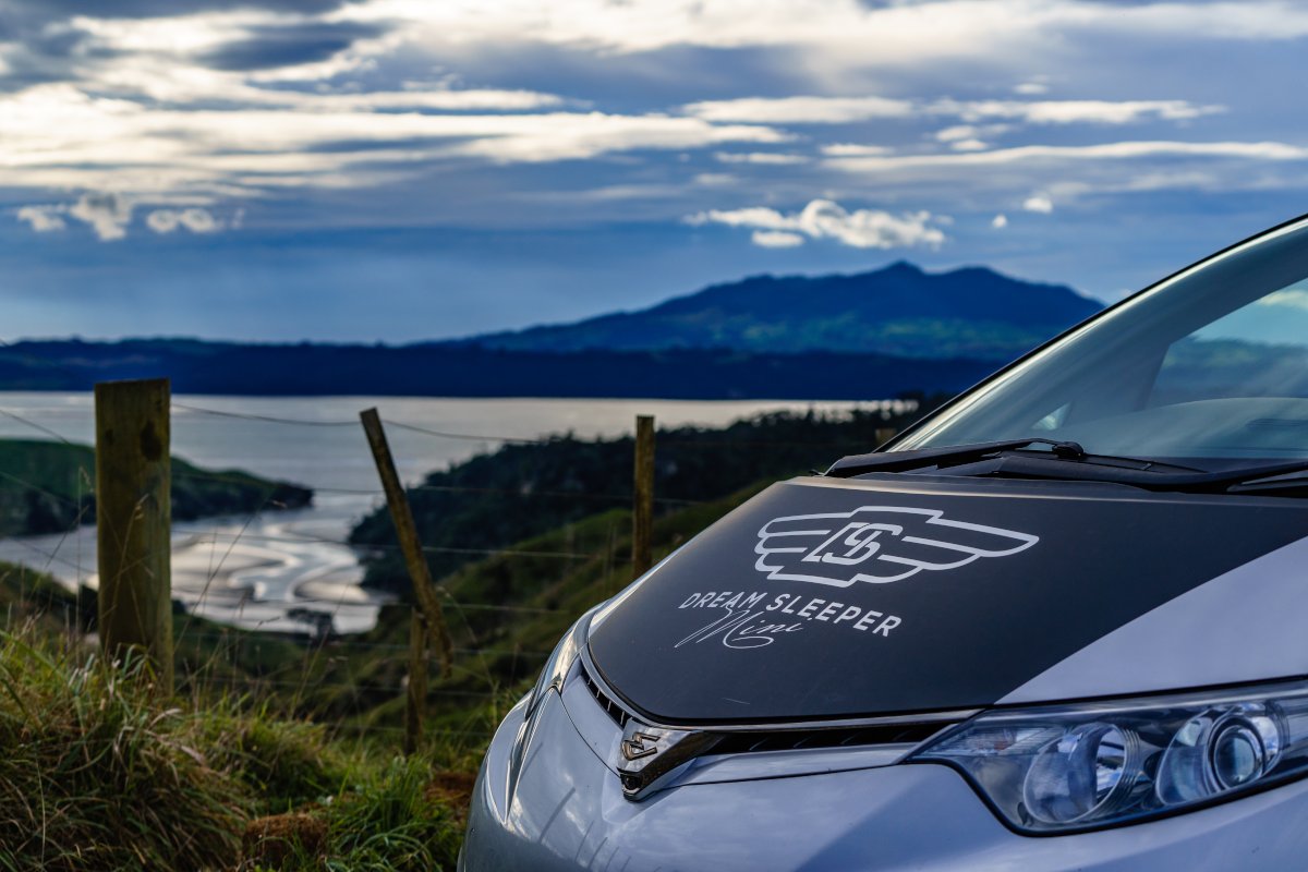 Front bonnet of a campervan parked at a lookout on a hill overlooking a harbour and rolling hills