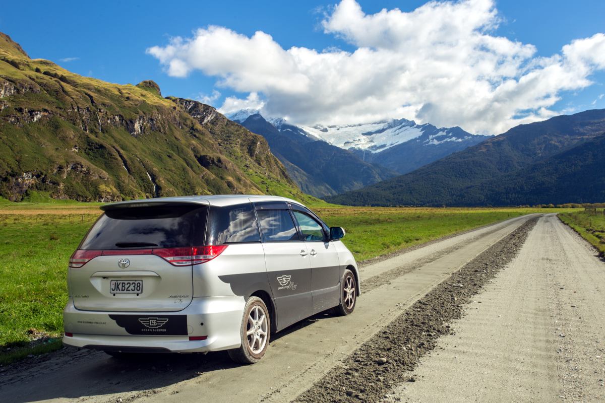 campervan driving on a rural gravel road towards a mountain range