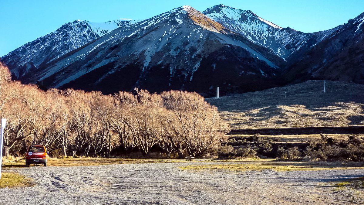 Lake Pearson campsite in winter: snow-dusted mountains in front, frostty campground in front - small campervan in distance