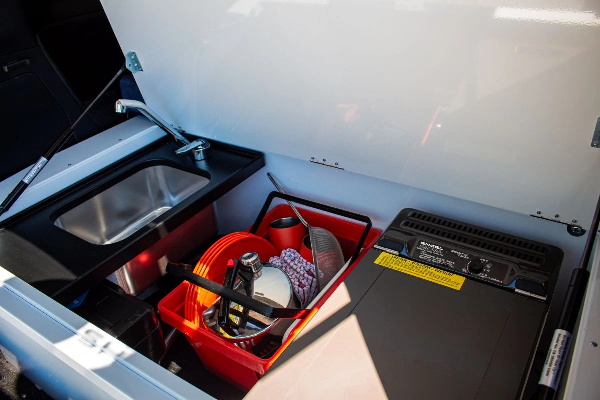 Kitchen set up in the rear of a campervan with a fridge, cooking gear and a sink
