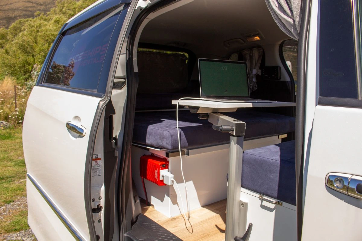 campervan door slid open showing a laptop charging set up at an adjustable table and bench seat