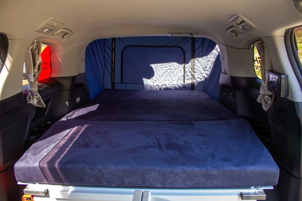 Interior bed set up of a campervan with blue mattresses laid out for the bed