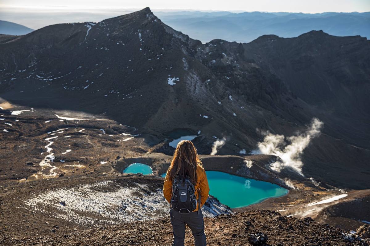 Tongariro Crossing: traveller standing on hill looking over the crossing and a lake in front of them | Photo: NZ dot com - Graeme Murray