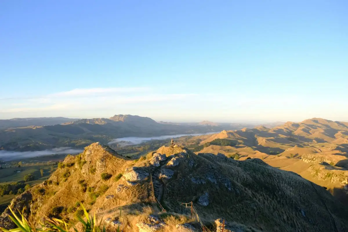Person standing on the very top of a hill with rural famrland surrounding them